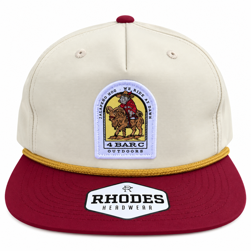 A structured baseball cap with an off-white crown and a dark red visor, featuring a gold braided trim along the edge. The front crown has a white patch with a cartoon biker on a horse, and the visor has a white patch for Rhodes Headwear. 4 Bar C Outdoors Jalapeño Hog cream and burgundy Rhodes rope hat with We Ride at Dawn patch